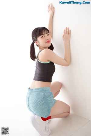 A young woman leaning against a white wall.