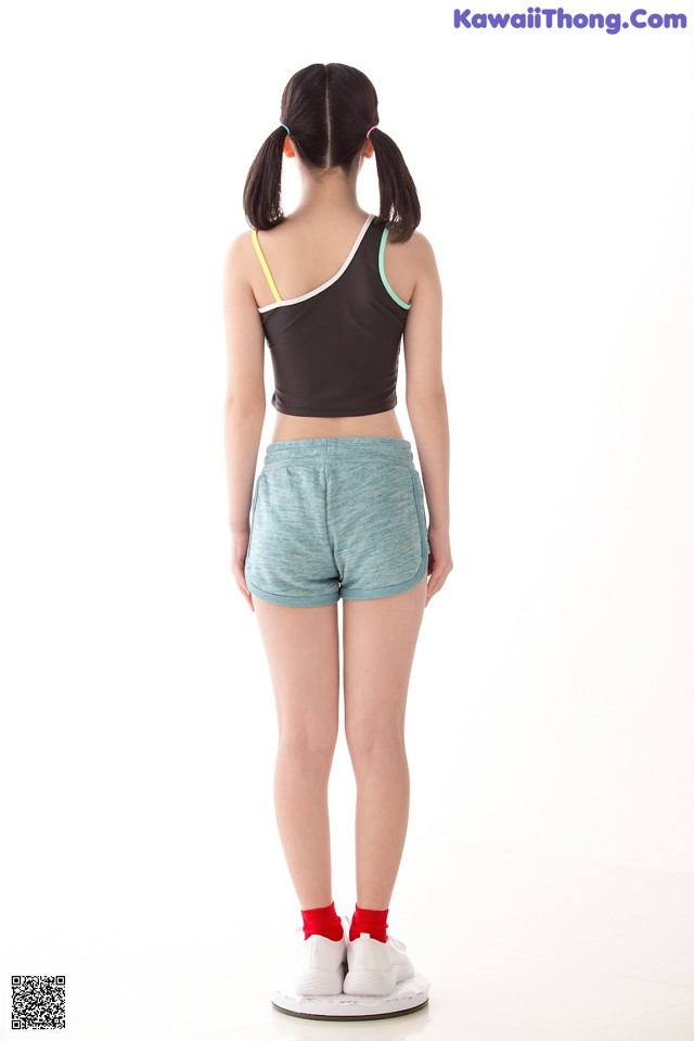 A young girl standing on a scale wearing a black top and blue shorts.