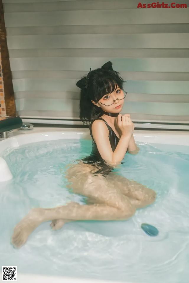 A woman in a black bathing suit sitting in a bathtub.