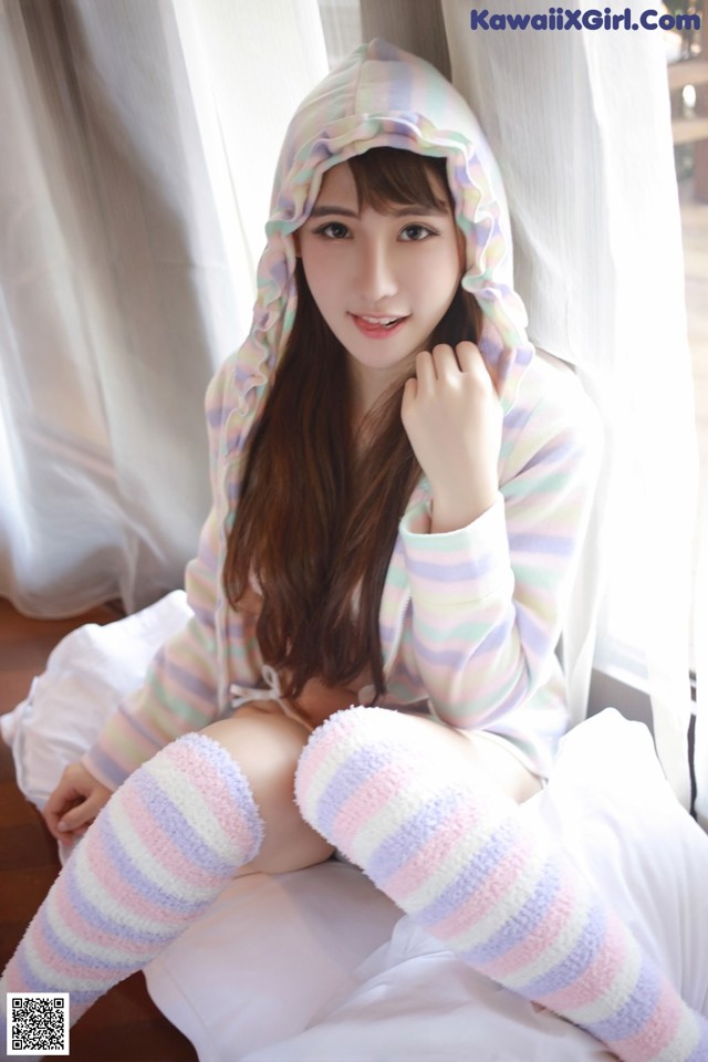 A woman in a striped hoodie sitting on a bed.