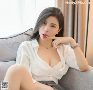 A woman in a white shirt and gray skirt sitting on a bed.