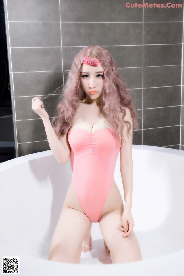 A woman in a pink bathing suit sitting in a bathtub.