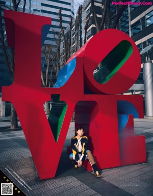 A woman sitting in front of a large red love sculpture.