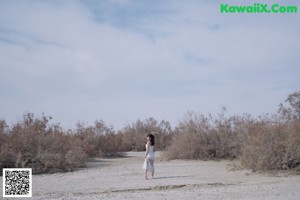 A woman in a white dress standing under a tree.