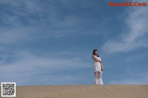 A woman in a white dress sitting on a sandy beach.