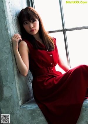 A woman in a white dress leaning against a wall.