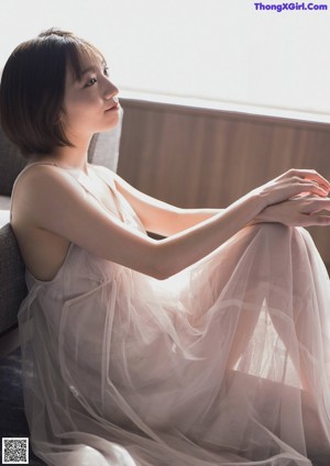 A woman in a white robe sitting on a window sill.