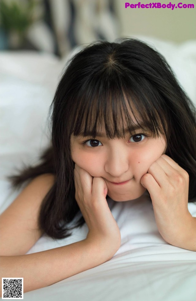 A young girl laying on a bed with her hand on her chin.