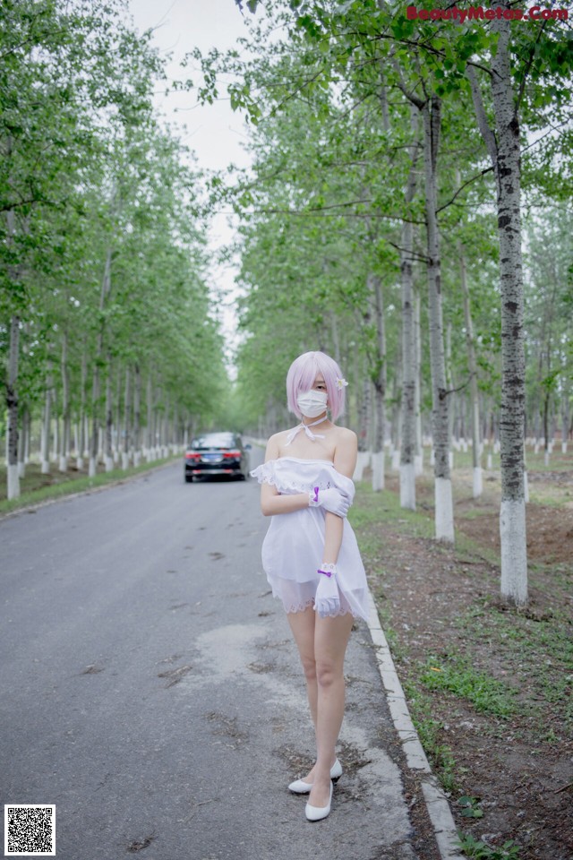 A woman in a white dress standing on the side of a road.