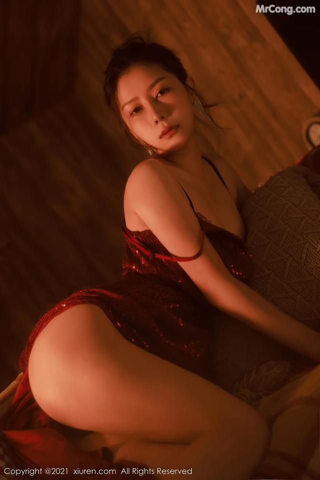 A woman in a red dress sitting on a bed.