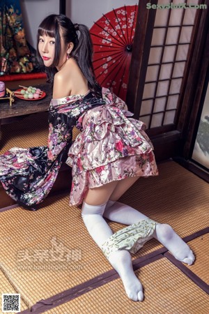 A woman in a kimono sitting on the floor next to a lamp.