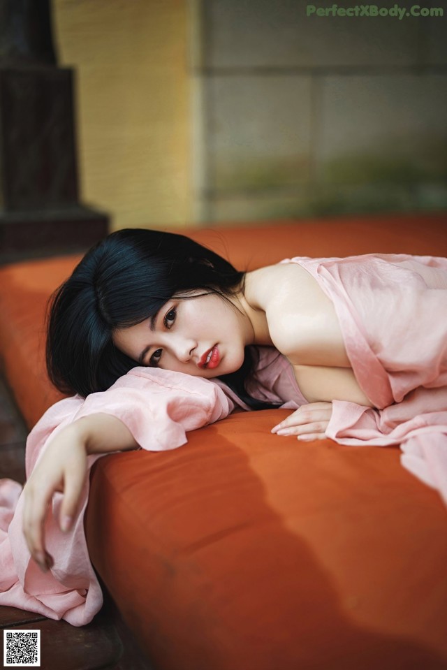 A woman in a pink dress laying on a red couch.