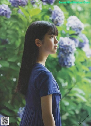 A young woman in a blue dress sitting on the ground.