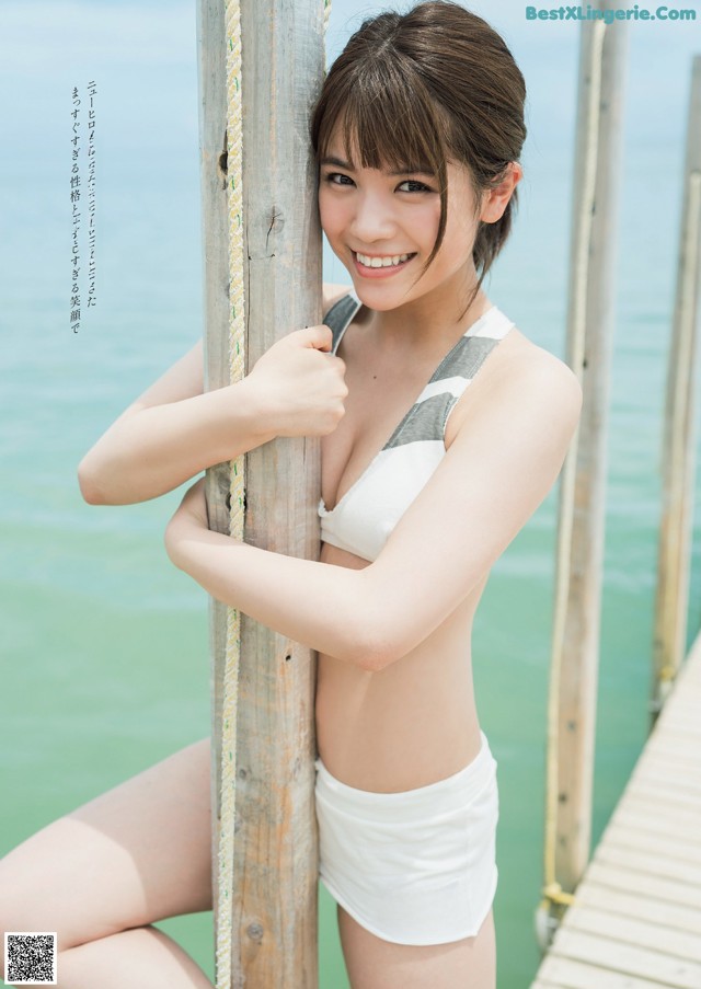 A woman in a white bikini leaning against a wooden pole.