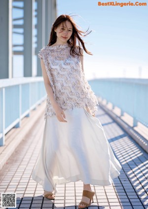 A woman in a white dress standing on a bridge.