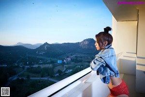 A woman in a denim jacket and red panties posing on a balcony.