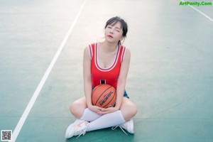 A woman in a red shirt and denim shorts holding a basketball.