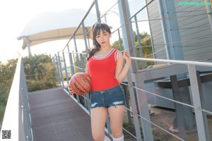 A woman in a red shirt and denim shorts holding a basketball.