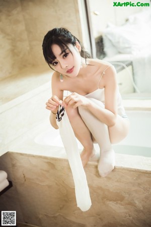 A woman in a white bodysuit posing on a bed.
