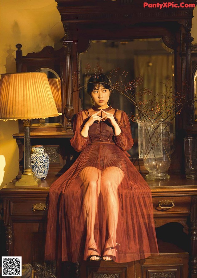 A woman sitting on top of a dresser next to a lamp.