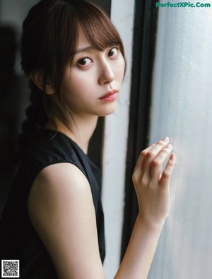 A woman in a black dress standing in front of a window.