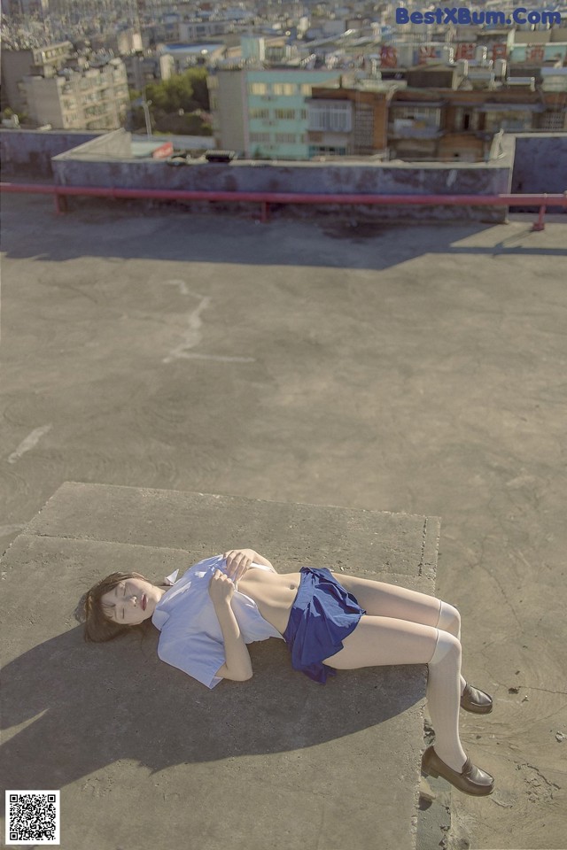 A woman laying on top of a building with a city in the background.
