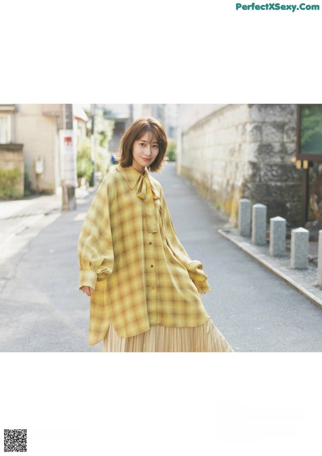 A woman in a yellow plaid shirt is walking down the street.