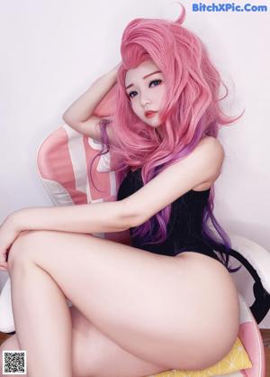 A doll with long pink hair sitting on a chair.