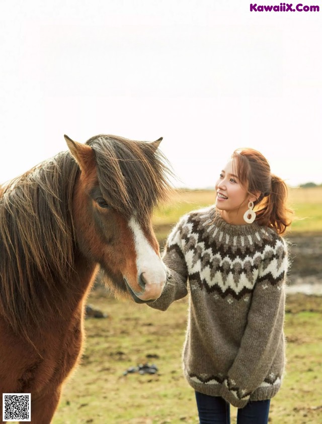 A woman standing next to a brown horse in a field.