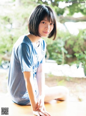 A young woman in a school uniform crouching on the beach.