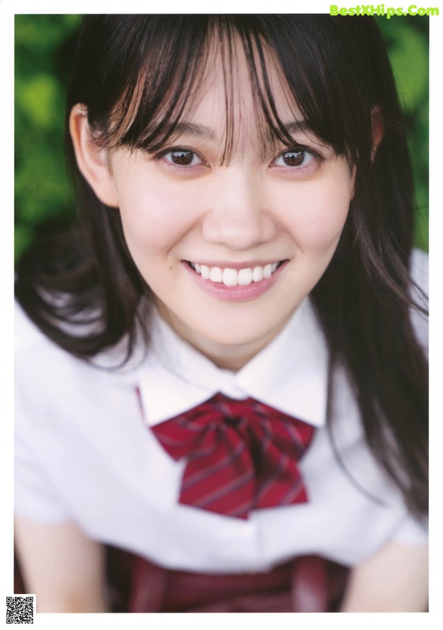 A woman in a school uniform smiles at the camera.