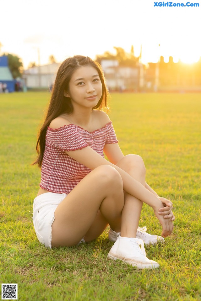 A woman sitting on the grass in a field at sunset.