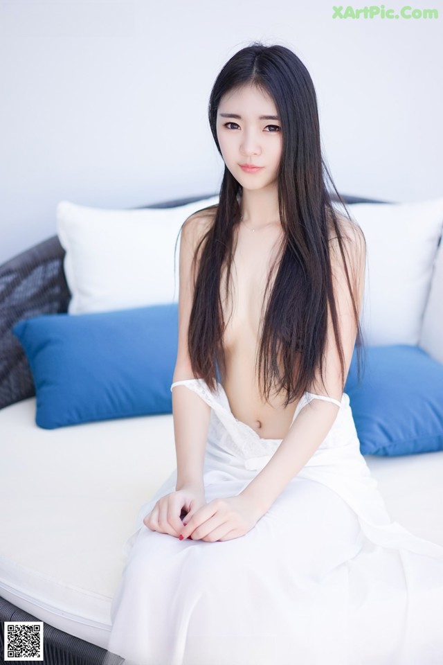 A woman in a white dress sitting on a bed.