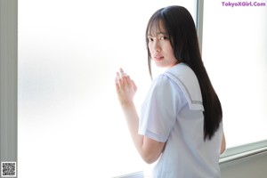 A woman in a school uniform standing by a window.