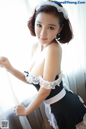 A woman in a maid outfit sitting on a bed.