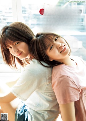 Two young women standing next to each other in front of a window.